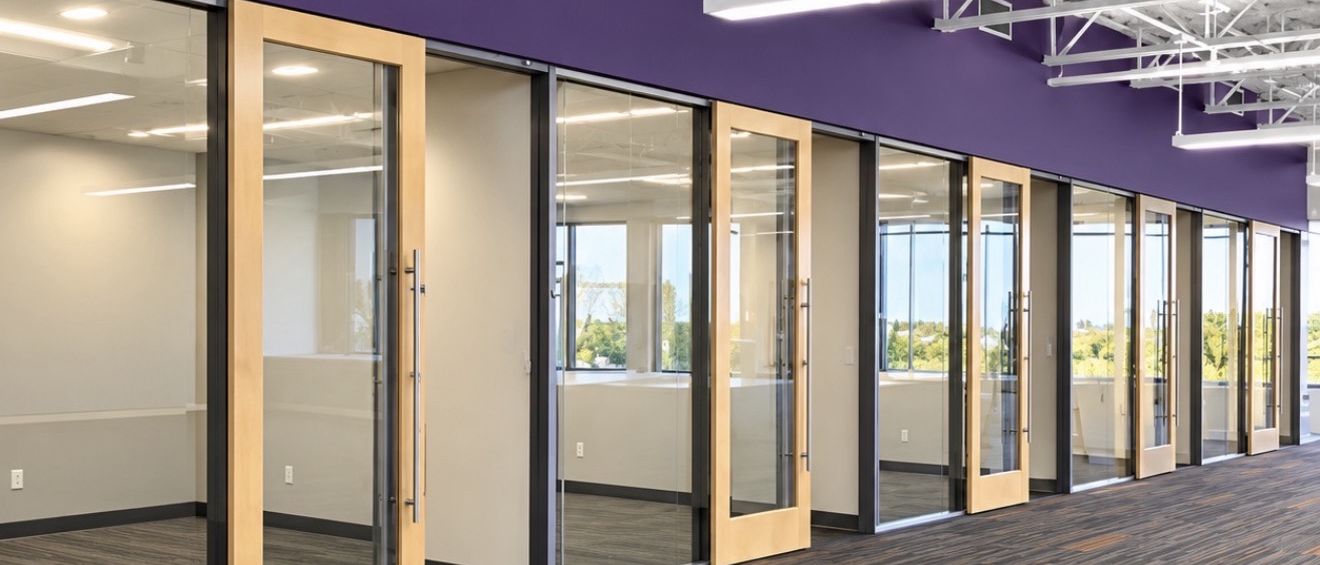 Completed office corridor with glazed private offices, exposed structure and ductwork, and new carpet tile.
