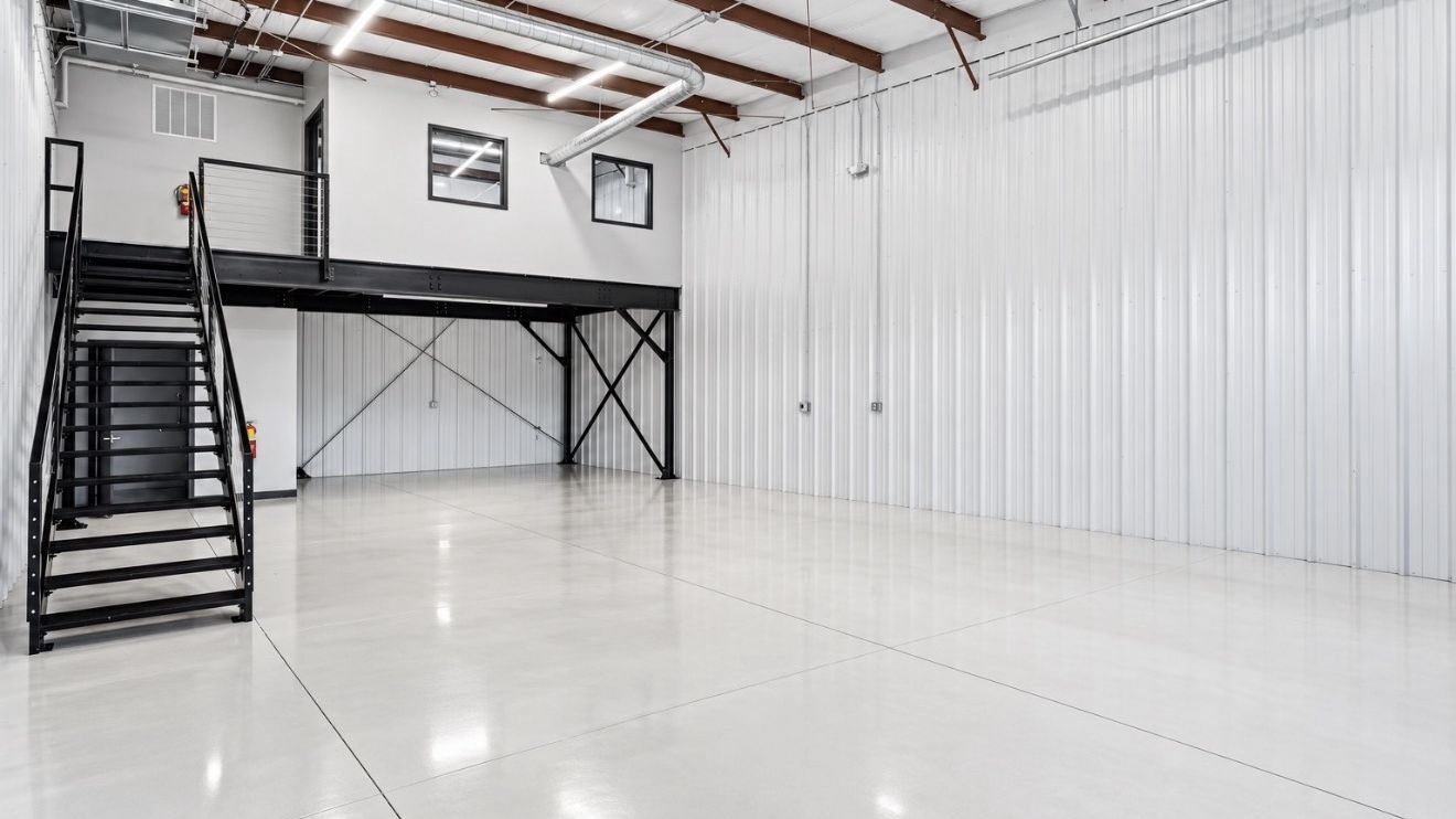 Completed industrial suite with a black steel mezzanine and staircase, white metal wall panels, and a polished concrete floor.