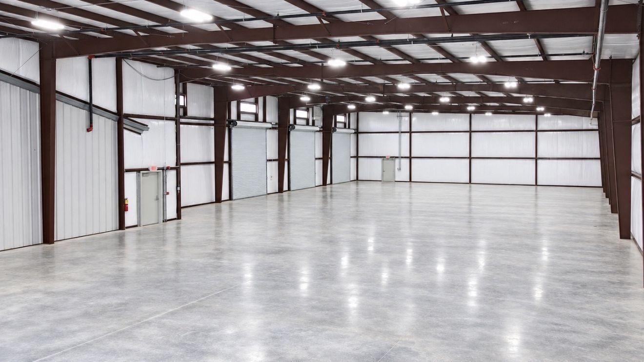 Finished industrial building interior with exposed steel frame, roll-up doors, and polished concrete floor.